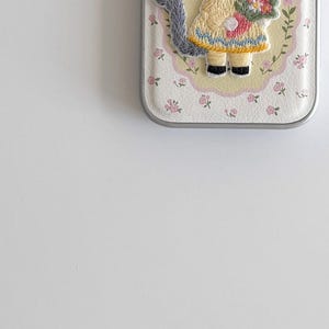 a phone case with a small embroidered design of a person wearing a yellow dress and holding a flower.