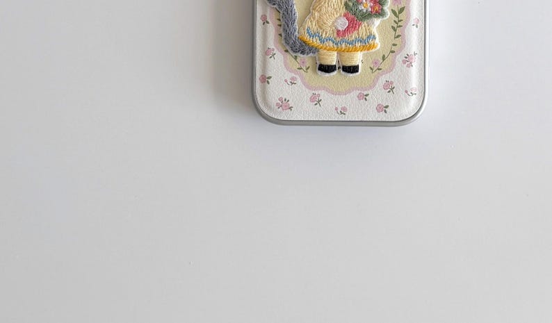 a phone case with a small embroidered design of a person wearing a yellow dress and holding a flower.