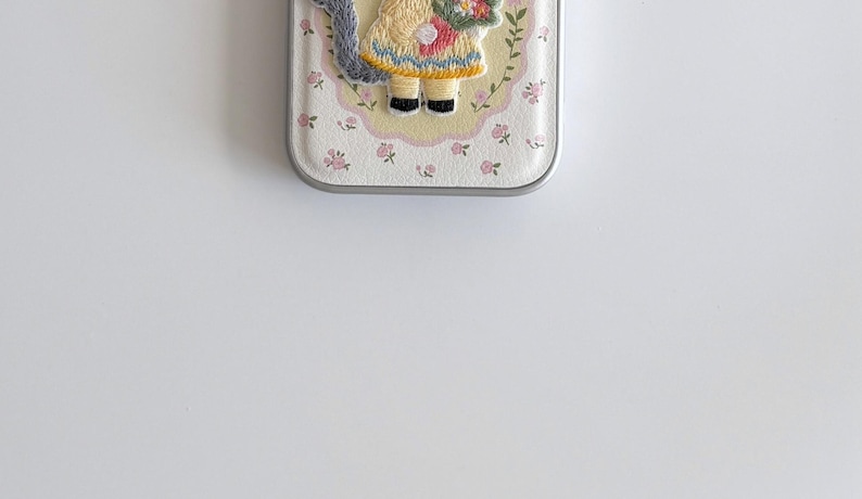 a small, decorative case with a floral pattern and a small figure of a person wearing a yellow dress.