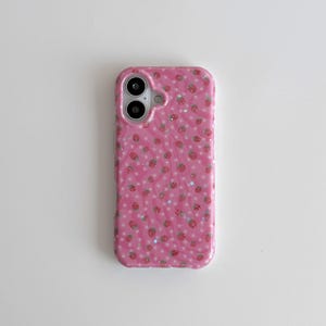 Könnte beinhalten: Rosa Handyhülle mit Erdbeer- und Sternmuster. Die Hülle hat eine glänzende Oberfläche und einen Kameraausschnitt. Das Design zeigt kleine rote Erdbeeren und silberne Sterne auf rosa Hintergrund.
