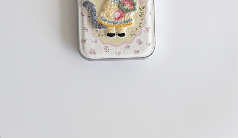 a small, white, floral-patterned case with a cat design on it, placed on a white surface.