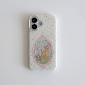 Könnte beinhalten: Weißes Handycase mit rosa Blumenmuster und einer gerahmten Illustration von Bambi und seinen Freunden. Das Case hat einen transparenten Glitzerrahmen um die Kameralinsen.