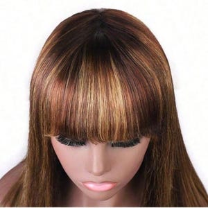 May include: A brown wig with blonde highlights and a dark root. The wig features a blunt bang and long, straight hair. The wig is styled on a mannequin head with a neutral skin tone.