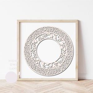 May include: A light beige, laser-cut wooden wreath with a floral and leaf design, framed in a light wood frame. The wreath is circular with a large open center. The background is white, and the floor is light wood.