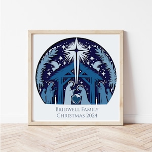 May include: A framed paper art piece in blue tones, featuring a nativity scene with a star and doves. The text reads "BRIDWELL FAMILY CHRISTMAS 2024". The artwork is layered and set against a white background.