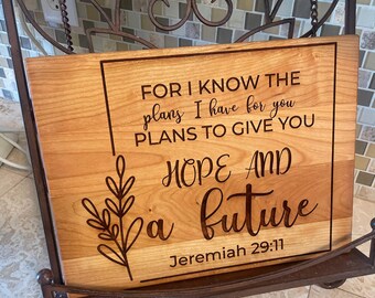 May include: Wooden sign with the text "FOR I KNOW THE plans I have for you PLANS TO GIVE YOU HOPE AND a future Jeremiah 29:11". The sign is light brown with a dark brown border and text.