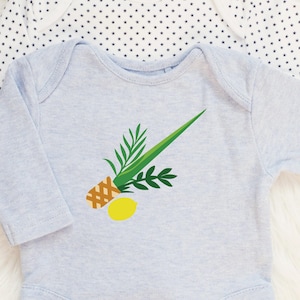 Puede incluir: Un body de bebé azul claro con un gráfico de piña, hojas verdes y un limón amarillo. El body está hecho de material suave y tiene mangas largas. El fondo es una superficie blanca con un patrón de estrellas.