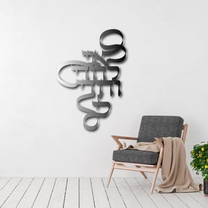 Peut inclure: Une œuvre d'art murale en métal avec une police cursive, avec un dégradé d'argent à noir. L'œuvre est montée sur un mur blanc, avec un fauteuil gris et une couverture en arrière-plan. Une petite plante en pot est également visible.