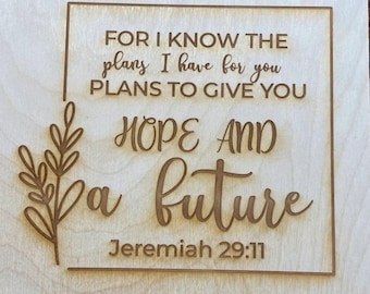 May include: Wooden sign with the quote "FOR I KNOW THE plans I have for you PLANS TO GIVE YOU HOPE AND a future Jeremiah 29:11". The text is in a brown color, with a decorative leaf design on the left side.