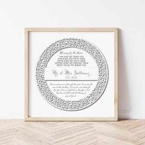 May include: A framed print with a white circular design featuring text in Hebrew and English. The text includes "Blessing for the Home" and "Mr. & Mrs. Gullman EST. 2023". The frame is a light wood color.