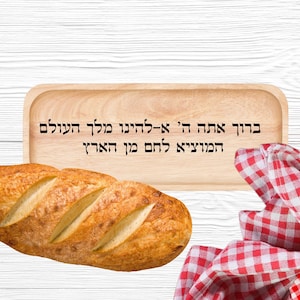 May include: A crusty loaf of bread with a golden-brown crust, displayed on a wooden tray with Hebrew text. A red and white checkered cloth is partially visible. The tray has Hebrew text.