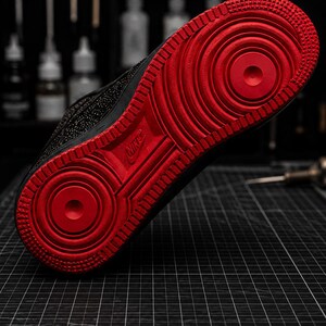 May include: Black and red Nike Air Force 1 sneaker. The sole is a vibrant red with a textured pattern, while the upper part of the shoe is black. The Nike logo is visible on the sole. This athletic shoe is designed for comfort and style.