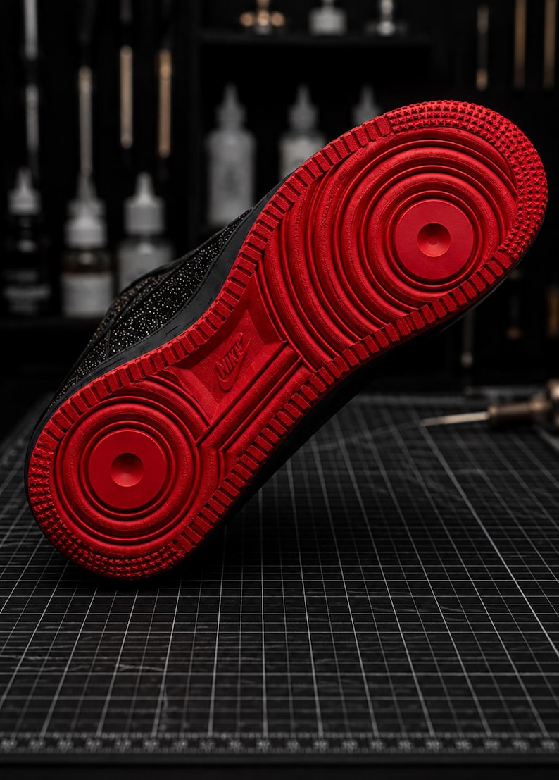 May include: Black and red Nike Air Force 1 sneaker. The sole is a vibrant red with a textured pattern, while the upper part of the shoe is black. The Nike logo is visible on the sole. This athletic shoe is designed for comfort and style.