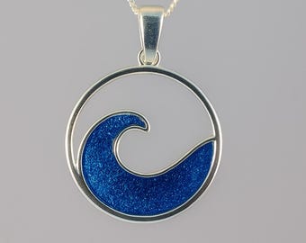 Può includere: Collana color argento con un ciondolo circolare con un motivo a onda. L'onda è riempita di materiale blu scintillante, creando un contrasto con il contorno e la catena argentati. Un gioiello semplice ed elegante.
