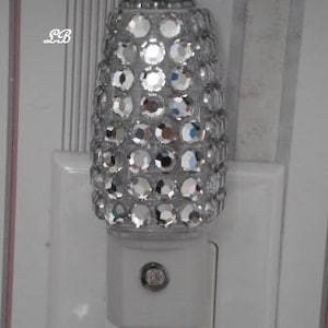 May include: A clear glass nightlight with a decorative diamond-like pattern. The nightlight is plugged into a standard electrical outlet.