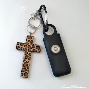 May include: A leopard print wooden cross keychain with a black flashlight attached to a silver carabiner.