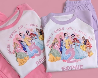 May include: Two sets of children's pajamas. One set is pink with a white top featuring a princess graphic and the number 5. The other set is lavender with a white top featuring a princess graphic and the number 2, with the name "Sophie".