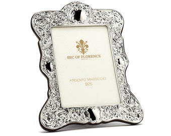 May include: Silver picture frame with an ornate design. The frame has a white mat with the text "SEC OF FLORENCE" and "ARGENTO MASSICCIO 925".