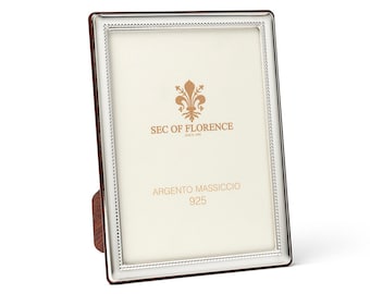 May include: A rectangular silver picture frame with a beaded border and a brown backing. The frame has the text "SEC OF FLORENCE" and "ARGENTO MASSICCIO 925" printed on the front.