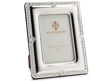 Puede incluir: Un marco de fotos de plata con un diseño ornamentado y un borde biselado. El marco tiene un pequeño soporte en la parte posterior y dice "SEC OF FLORENCE" y "ARGENTO MASSICCIO 925" en la parte delantera.