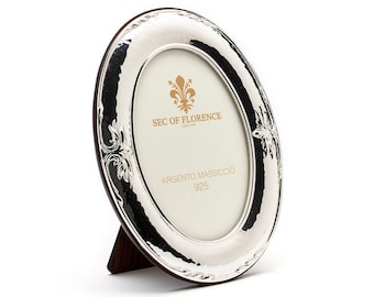 May include: Silver oval picture frame with an ornate design and a stand. The frame has the text "SEC OF FLORENCE" and "ARGENTO MASSICCIO 925" on it.