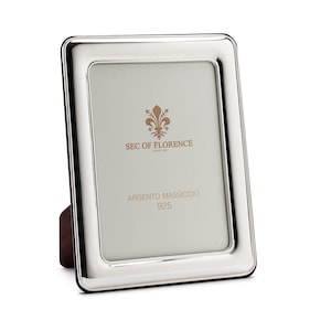 May include: A silver picture frame with a bevelled edge and a stand. The frame has the text "SEC OF FLORENCE" and "ARGENTO MASSICCIO 925" printed on it.