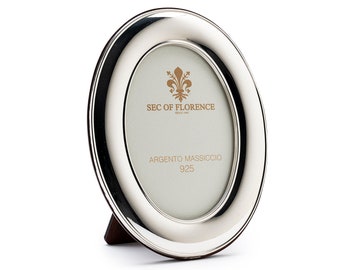 May include: Silver oval picture frame with a wooden stand. The frame has a raised edge and the inscription "SEC OF FLORENCE" and "ARGENTO MASSICCIO 925".