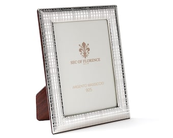 May include: Silver picture frame with a grid pattern and a wooden stand. The frame has the text "SEC OF FLORENCE" and "ARGENTO MASSICCIO 925" on it.