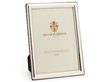 May include: A silver picture frame with a beveled edge and a white mat. The frame has the text "SEC OF FLORENCE" and "ARGENTO MASSICCIO 925" printed on it.