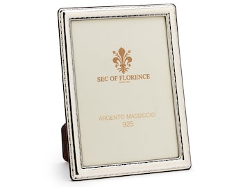 May include: A silver picture frame with a white mat and a silver border. The frame has a small stand on the back. The frame has the text "SEC OF FLORENCE" and "ARGENTO MASSICCIO 925" on the mat.
