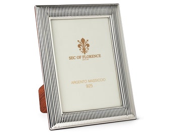 May include: A silver picture frame with a textured, striped design. The frame has a wooden stand and features the text "SEC OF FLORENCE" and "ARGENTO MASSICCIO 925".