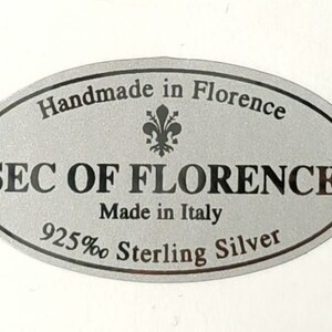 May include: A silver oval sticker with black text that reads "Handmade in Florence", a stylized fleur-de-lis, "SEC OF FLORENCE", "Made in Italy", and "925% Sterling Silver".