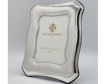 May include: A silver picture frame with a beveled edge and a black backing. The frame has the text "SEC OF FLORENCE since 1998" and "ARGENTO MASSICCIO 925" printed on it.