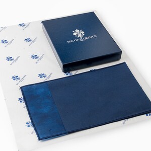 May include: A blue box with the text "SEC OF FLORENCE" on the top. The box is sitting on white tissue paper with a blue and white pattern. A blue cloth is next to the box.