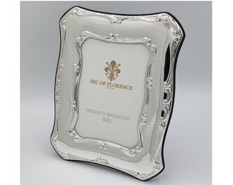 May include: A silver picture frame with an ornate design. The frame has a black backing and features the text "SEC OF FLORENCE" and "ARGENTO MASSICCIO 925".