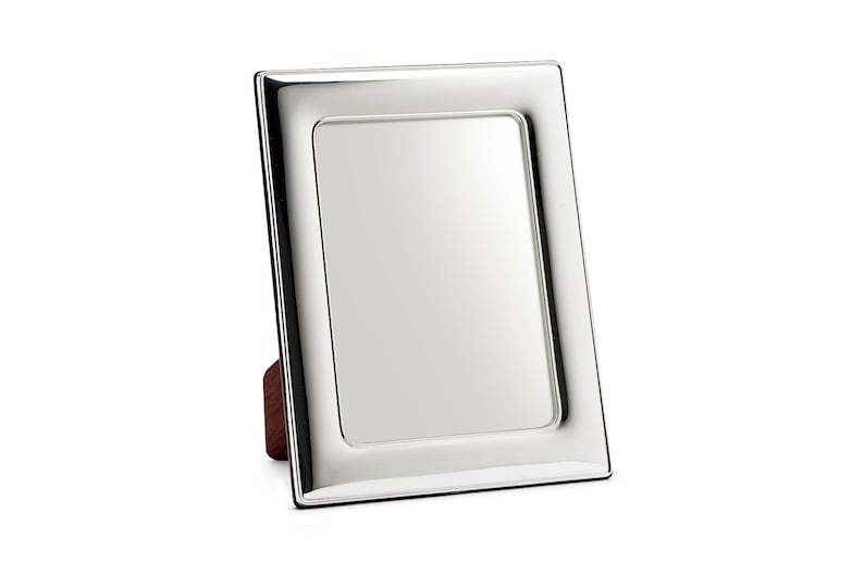 May include: A silver picture frame with a wood stand. The frame has a polished finish and a simple design.