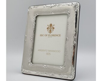Pode incluir: Uma moldura retangular prateada com textura martelada e detalhes ornamentados. A moldura tem um verso preto e apresenta o texto "SEC OF FLORENCE" e "ARGENTO MASSICCIO 925". A moldura foi projetada para conter uma fotografia ou obra de arte.