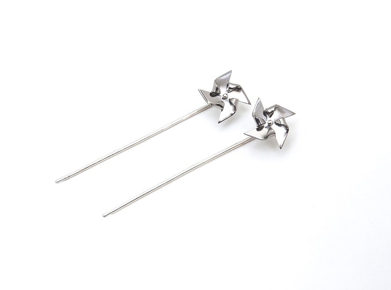 A pair of long pined Pinwheel earrings. They are ear jackets made with Titanium on the pinwheel part and Silver 925 pins and they can actually spin. They are silver colored with polished finish.