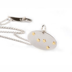 Oval shaped pendant that has two layers. The base is Silver 925 in bright matte finish and on it are the Cassiopeia constellation stars in solid Yellow Gold with polished finish. Hangs from a thin link silver 925 chain with a Largentolab clasp.