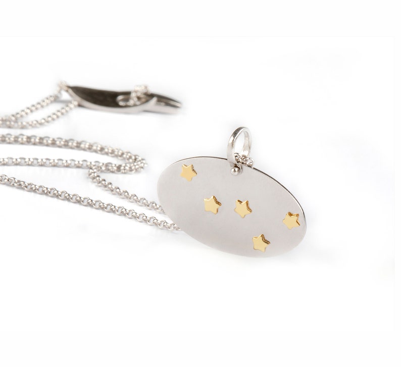 Oval shaped pendant that has two layers. The base is Silver 925 in bright matte finish and on it are the Cassiopeia constellation stars in solid Yellow Gold with polished finish. Hangs from a thin link silver 925 chain with a Largentolab clasp.