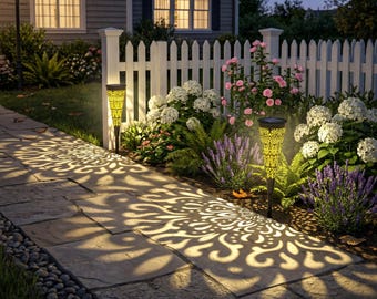 May include: Two solar-powered garden stake lights with intricate cut-out patterns that cast decorative, glowing floral-like shadows onto a stone walkway. The tall, tapered, dark-colored fixtures illuminate the surrounding garden beds.