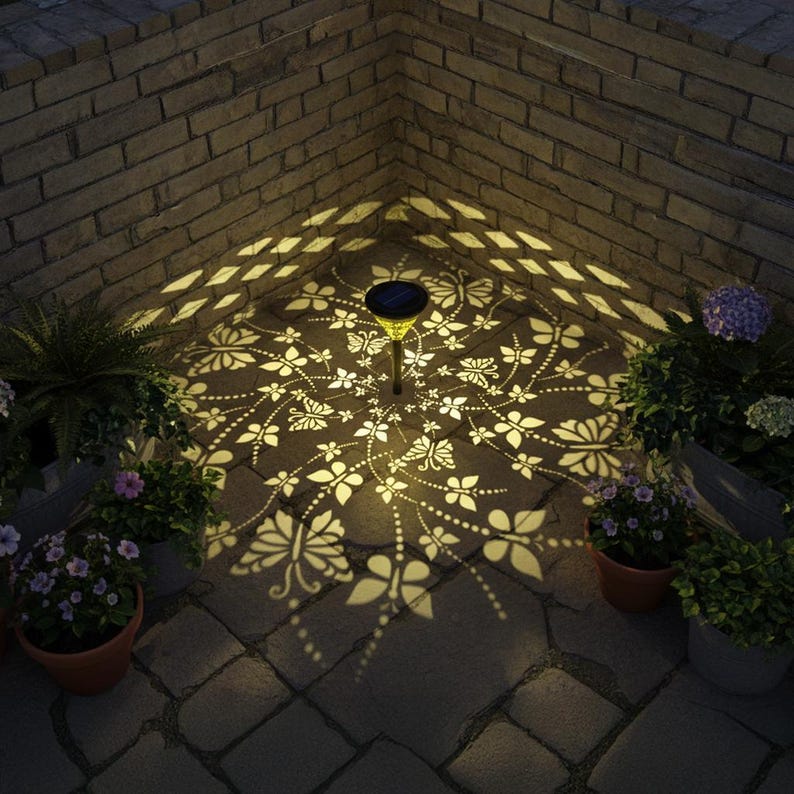 May include: A solar-powered garden light casts a butterfly and floral pattern on a brick patio. The light is surrounded by potted plants and is set against a brick wall. The light's glow creates a decorative ambiance.