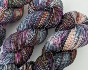 May include: Close-up of several skeins of hand-dyed yarn. The yarn is a mix of colors, including blues, purples, pinks, and yellows. The yarn is soft and appears to be made of a natural fiber. The skeins are arranged in a visually appealing way.