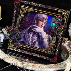 May include: A square black picture frame featuring a portrait of a person with long light purple hair, wearing a ruffled white shirt and gloves. The frame is decorated with gold filigree corners, red roses, and iridescent glitter accents.