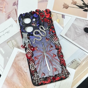Op de afbeelding: Een rechthoekig telefoonhoesje met een donkerpaars en glinsterend oppervlak, versierd met 3D-versieringen waaronder een zilveren slang, een centraal zwaard, een skeletachtige hand, een metalen hand, een rood anatomisch hart en rode rozen.