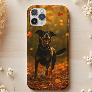 Pode incluir: Uma capa de telemóvel com um cão feliz a correr numa floresta com folhas de outono a cair. O cão é preto e castanho, com a língua de fora. O fundo é um borrão de cores de outono, com folhas vermelhas e laranja.