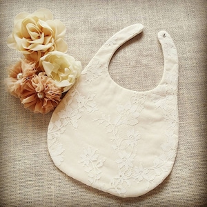 May include: A white lace bib with a floral pattern. The bib is made of a soft, lightweight fabric and has a simple design.