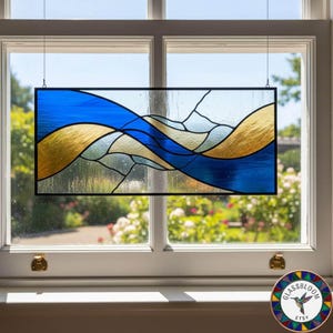 May include: Rectangular stained glass panel with a black frame, depicting a flowing design in blue and gold. The panel is suspended in front of a window. The design features abstract shapes, reminiscent of a landscape.
