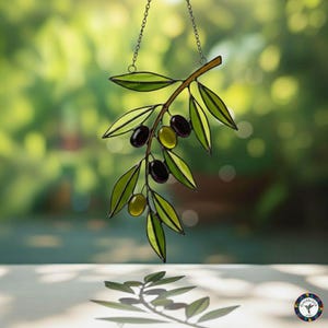 May include: Stained glass olive branch with green leaves and black and green olives, hanging from a chain. The artwork is set against a blurred green background, creating a natural and elegant aesthetic.