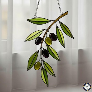 May include: Stained glass olive branch with green leaves and black and green olives. The branch is brown and hangs from a chain. The glass is outlined in black.